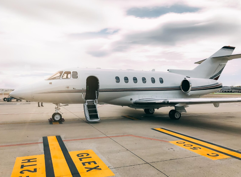 Private jet parked on runway at airport with open cabin door, highlighting hidden costs of private air travel like landing fees.