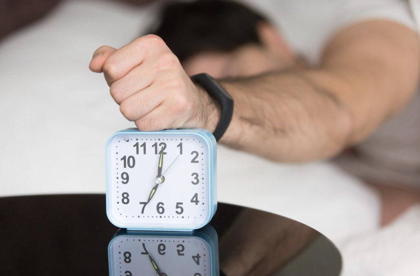 Man waking up in bed and reaching to turn off alarm clock to reset sleep schedule.