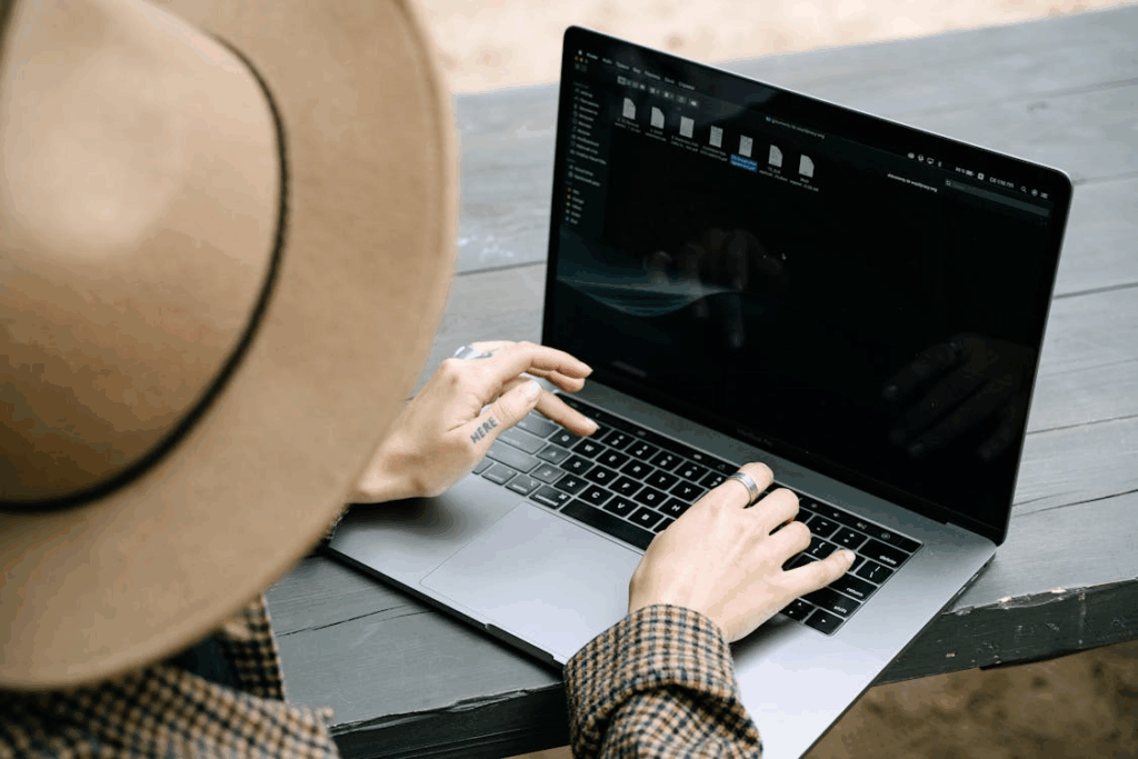 Person using a laptop in dark mode outdoors, typing on a MacBook with a dim screen interface.